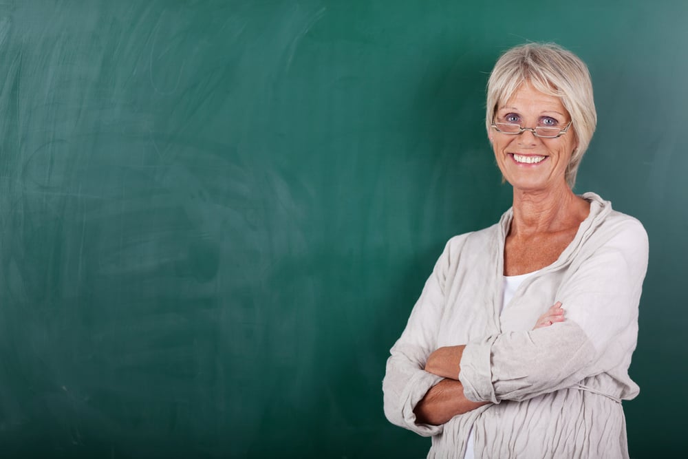 Portrait of happy senior female teacher with arms crossed standing against chalkboard Portrait of happy senior female teacher with arms crossed standing against chalkboard